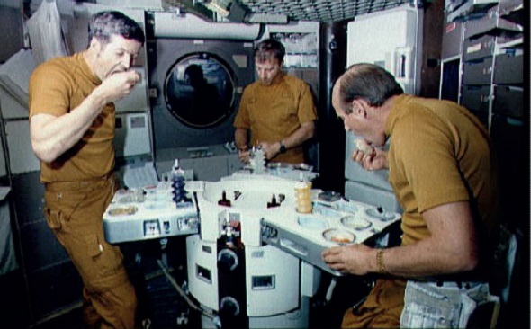 A Skylab crew eat from their trays at the Raymond Loewy-designed table in 1973. L-R: Joseph P. Kerwin, Paul J. Weitz and Charles Conrad Jr.